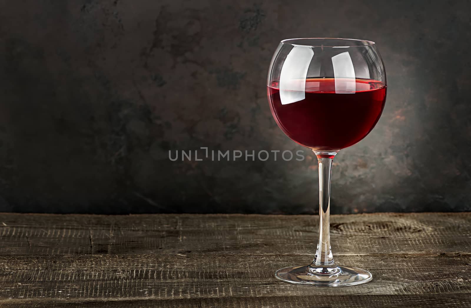 Glass of red wine on a wooden table. Dark blurry background.