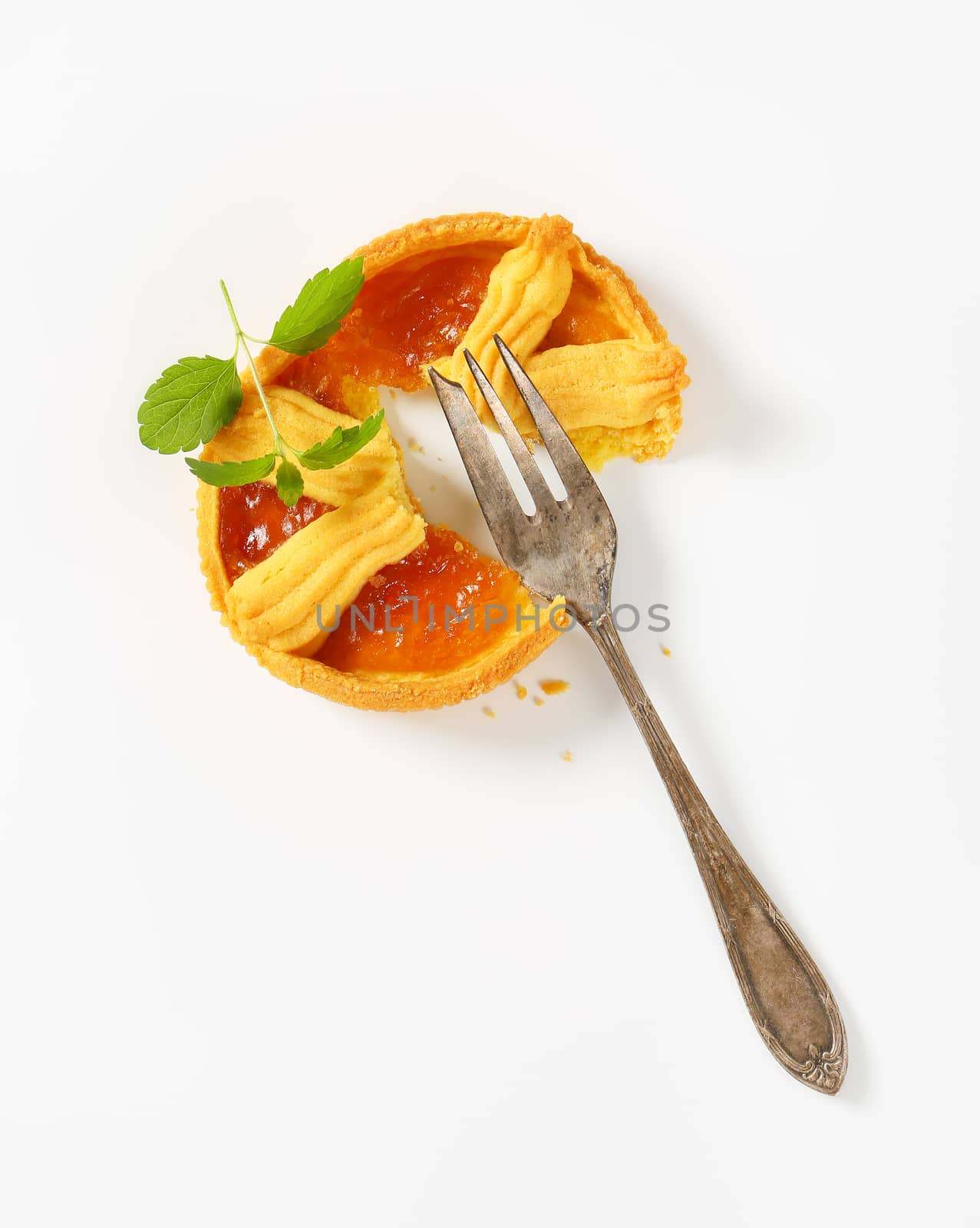 halved apricot jam tart and silver fork on white background