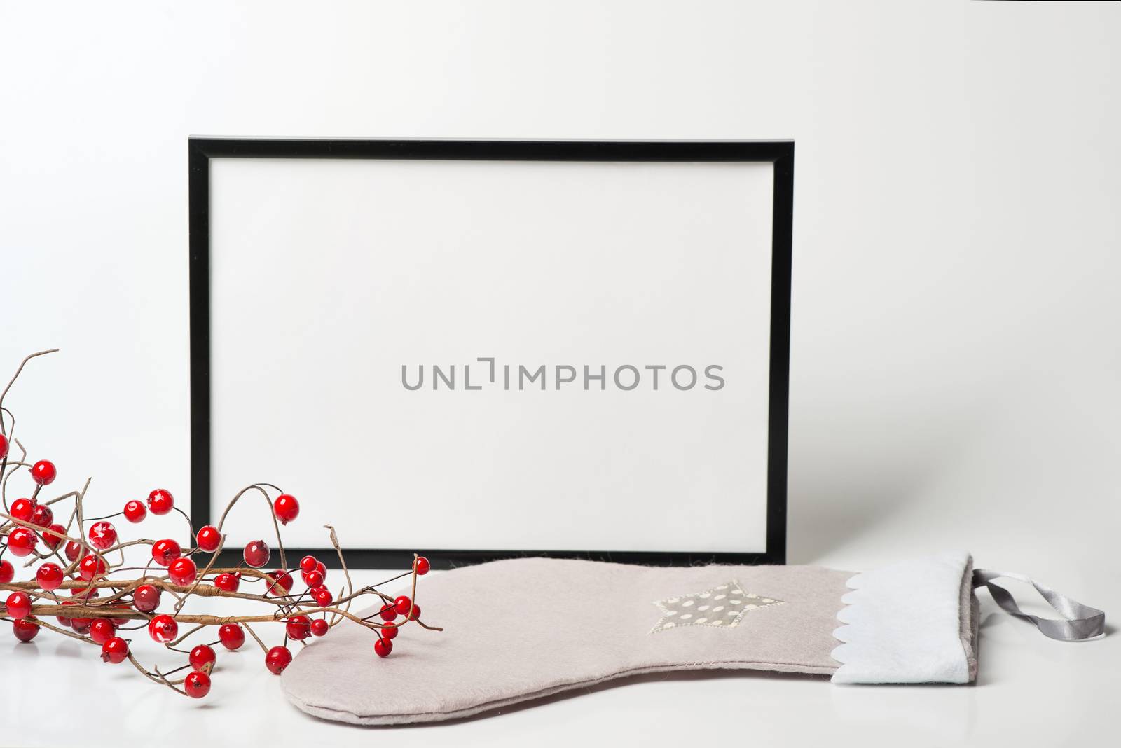 Christmas composition. Black frame and christmas sock with branches with red berries on white background. Front view, mock up, copy space, square, flat lay, for congratulations

