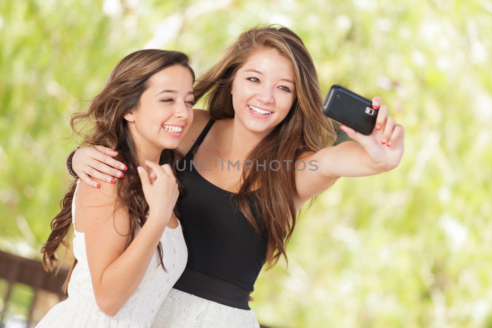 Two Attractive Mixed Race Girlfriends Using Their Smart Cell Phones For Selfie Outdoors by Feverpitched