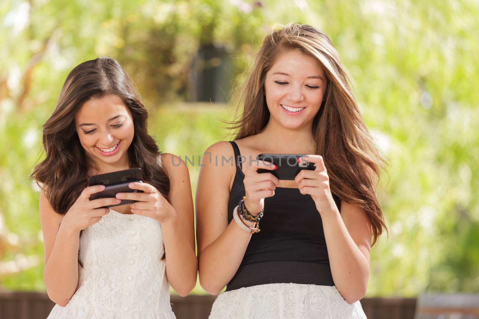 Two Expressive Mixed Race Girlfriends Using Their Smart Cell Phones Outdoors by Feverpitched