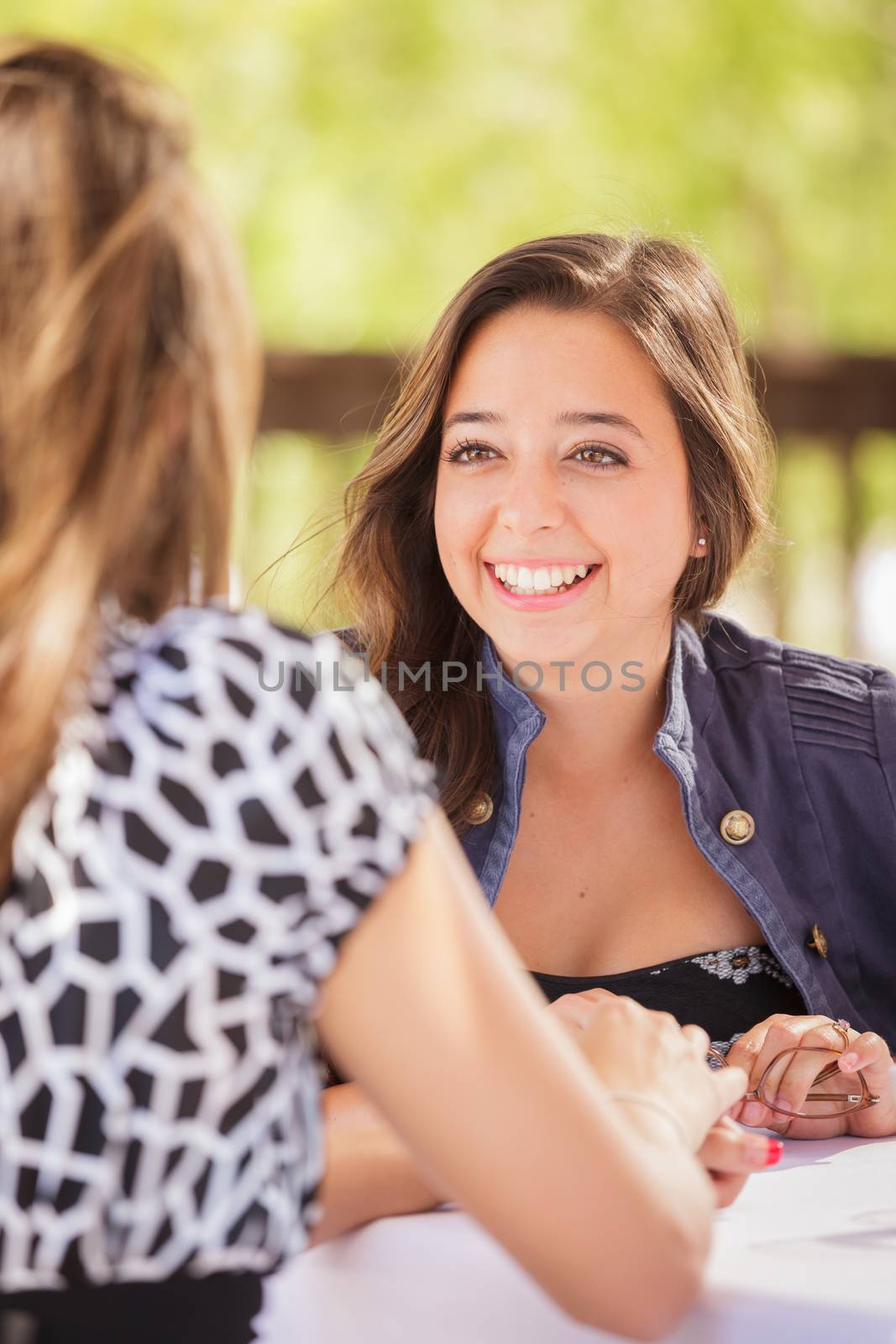 Two Mixed Race Girlfriends Having A Conversation At An Outoor Patio Table