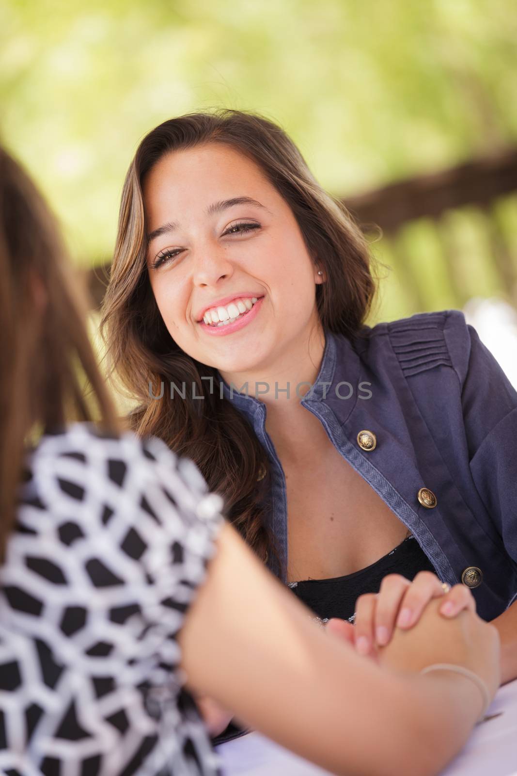 Two Mixed Race Girlfriends Having A Conversation At An Outoor Patio Table by Feverpitched
