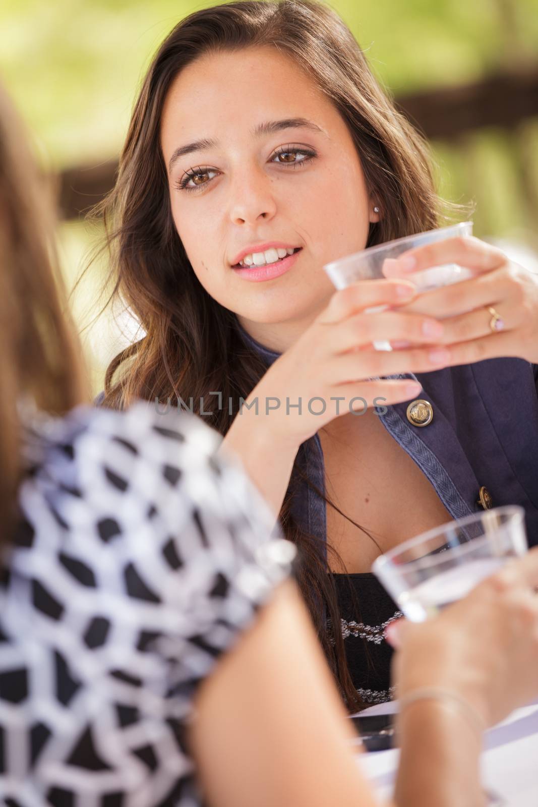 Expressive Young Adult Woman Having Drinks and Talking with Her Friend Outdoors by Feverpitched