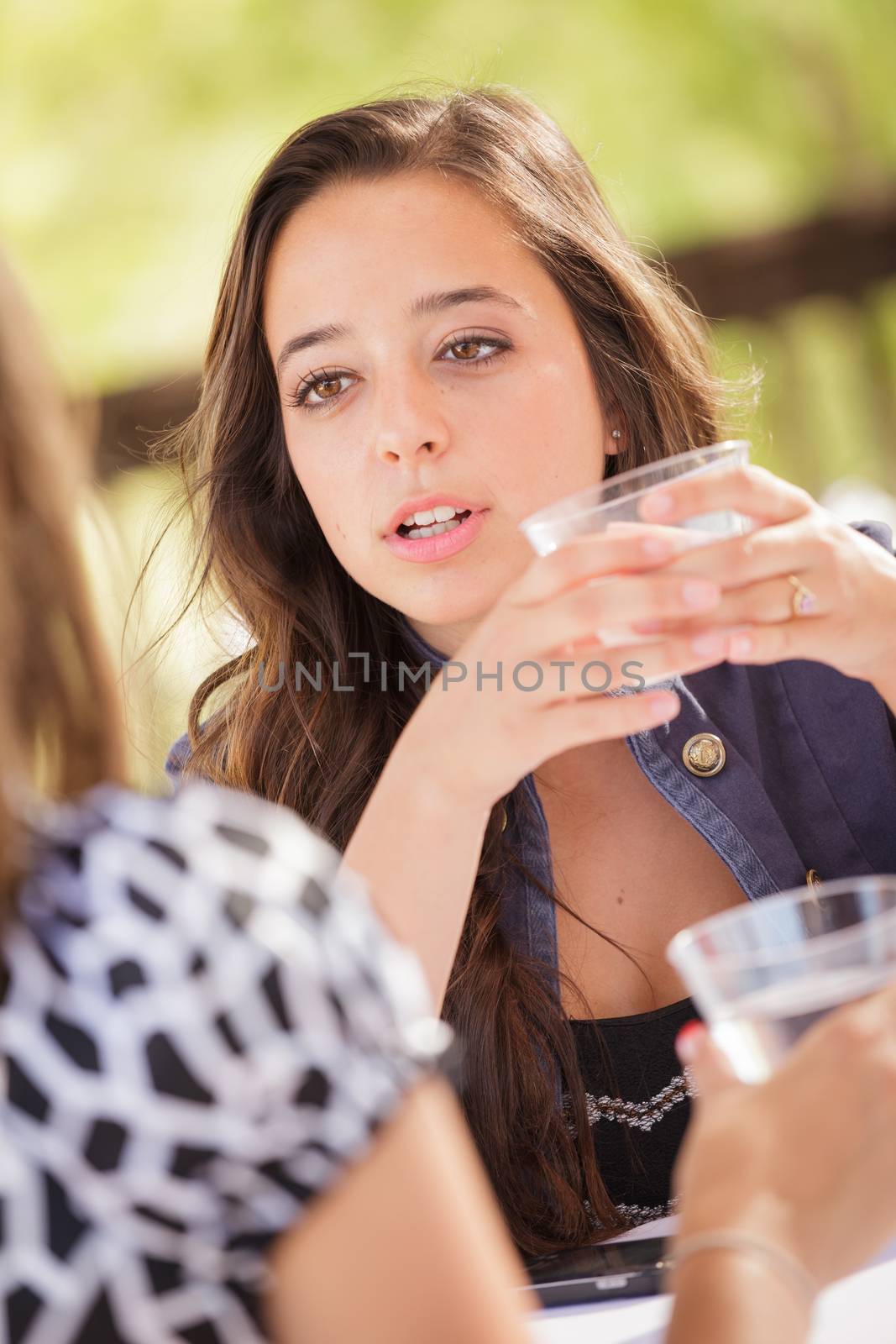 Expressive Young Adult Woman Having Drinks and Talking with Her Friend Outdoors