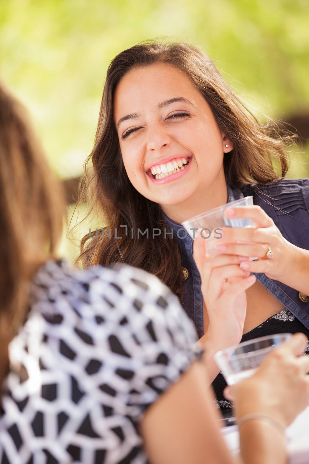 Expressive Young Adult Woman Having Drinks and Talking with Her Friend Outdoors by Feverpitched