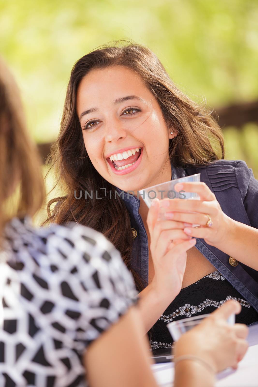 Expressive Young Adult Woman Having Drinks and Talking with Her Friend Outdoors