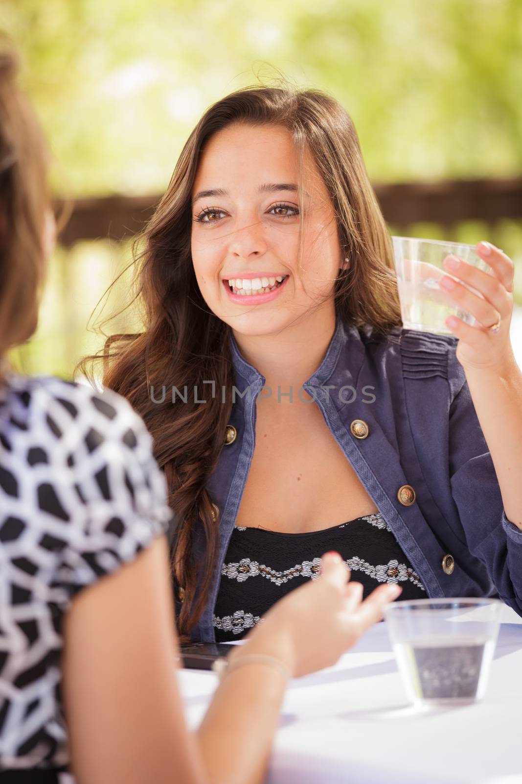 Expressive Young Adult Woman Having Drinks and Talking with Her Friend Outdoors by Feverpitched