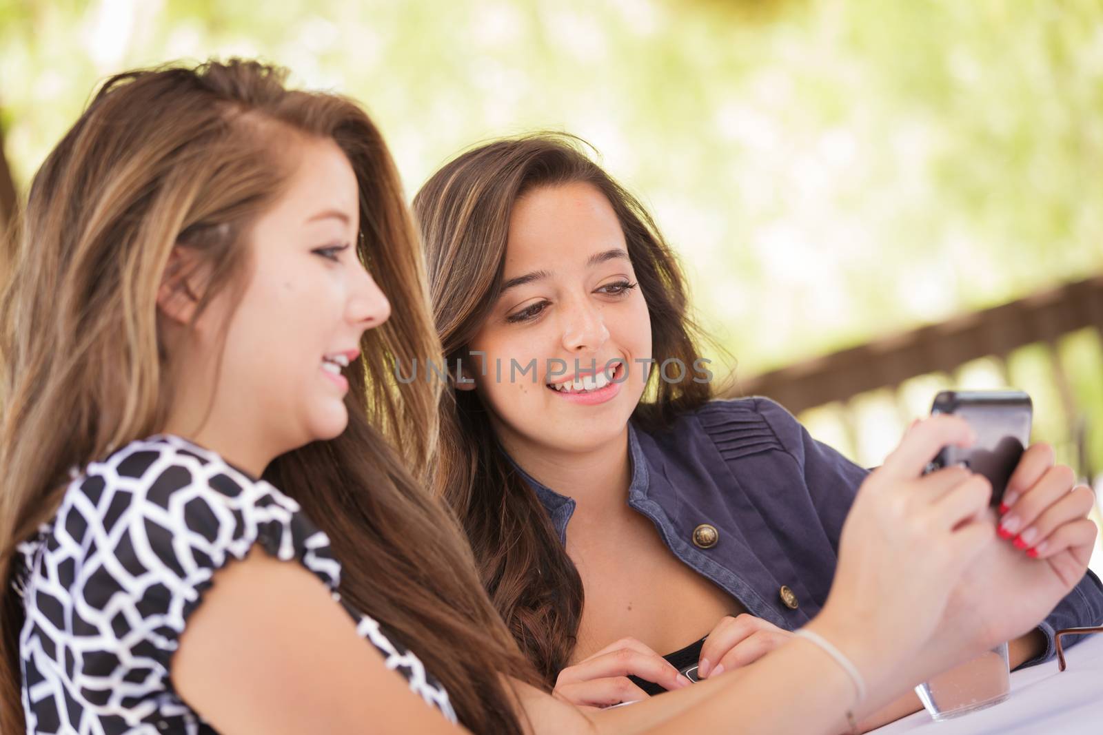 Expressive Young Adult Girlfriends Using Their Smart Cell Phone Outdoors by Feverpitched