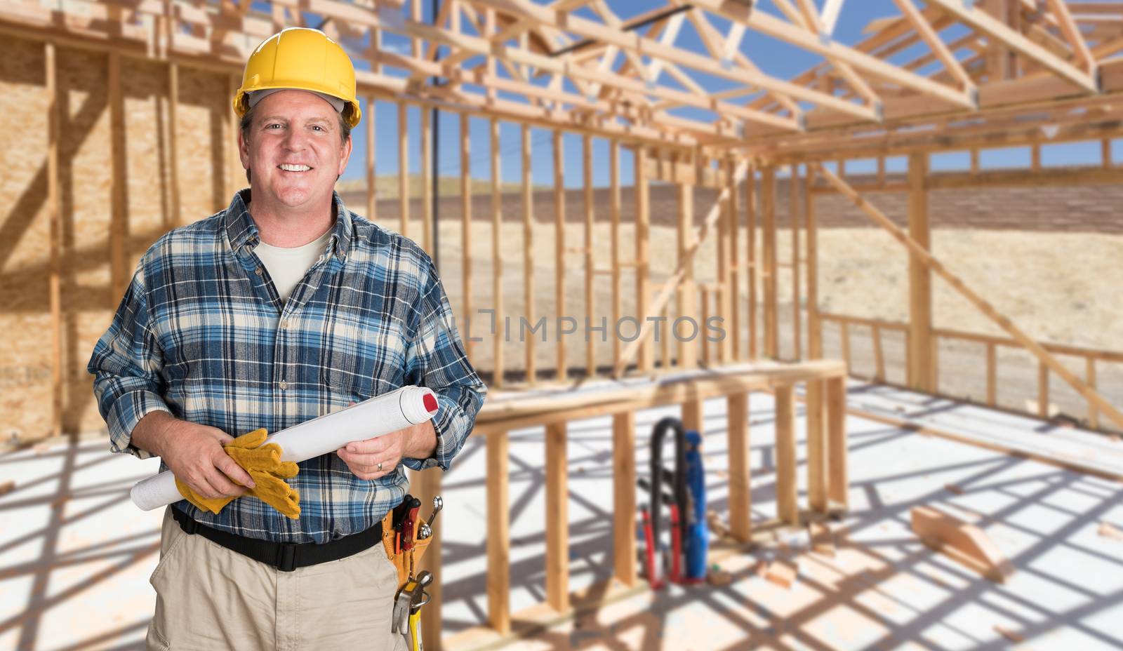 Male Contractor With House Plans Wearing Hard Hat Inside New House Construction Framing