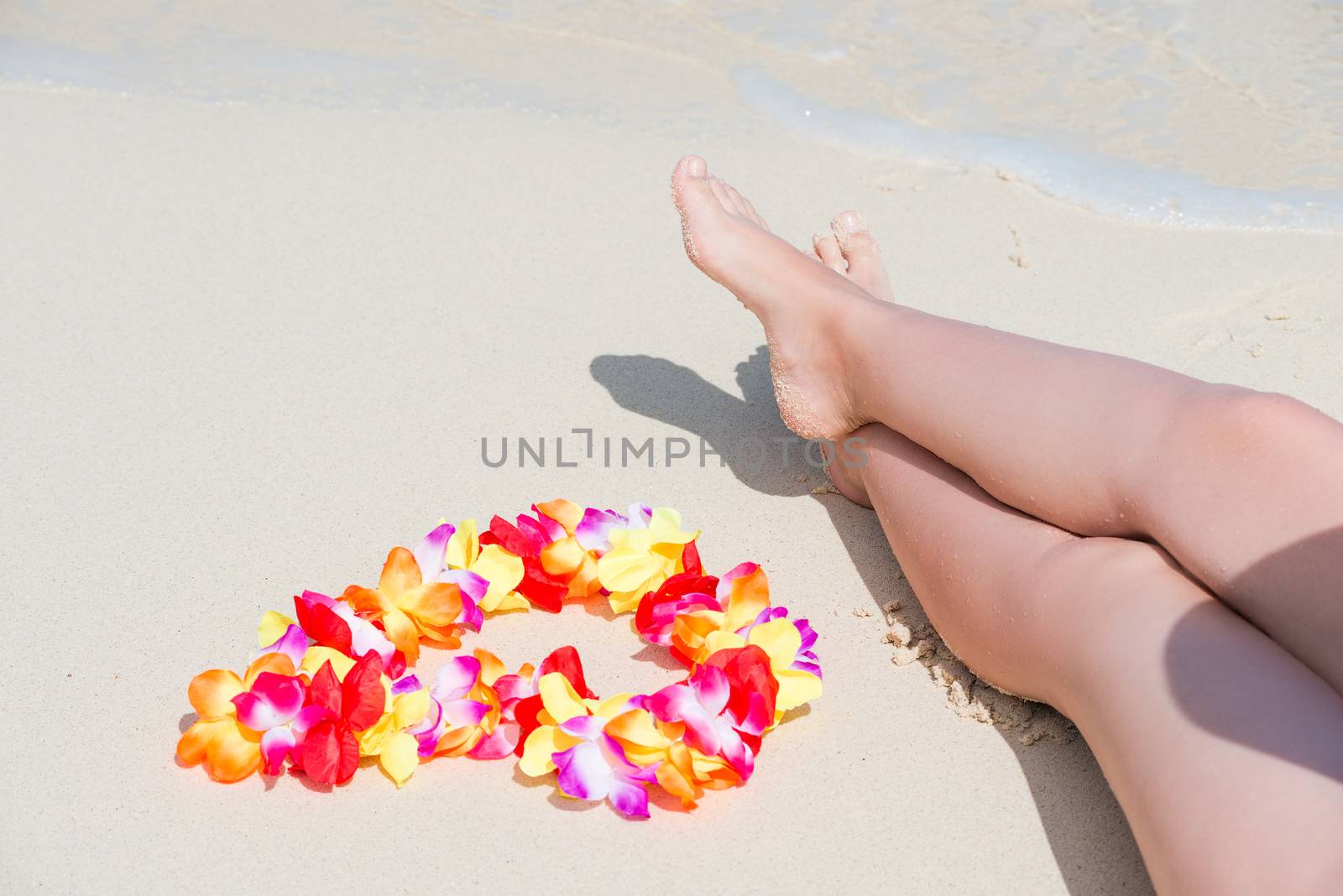 beautiful female legs on a sandy beach and Hawaiian Lei close-up