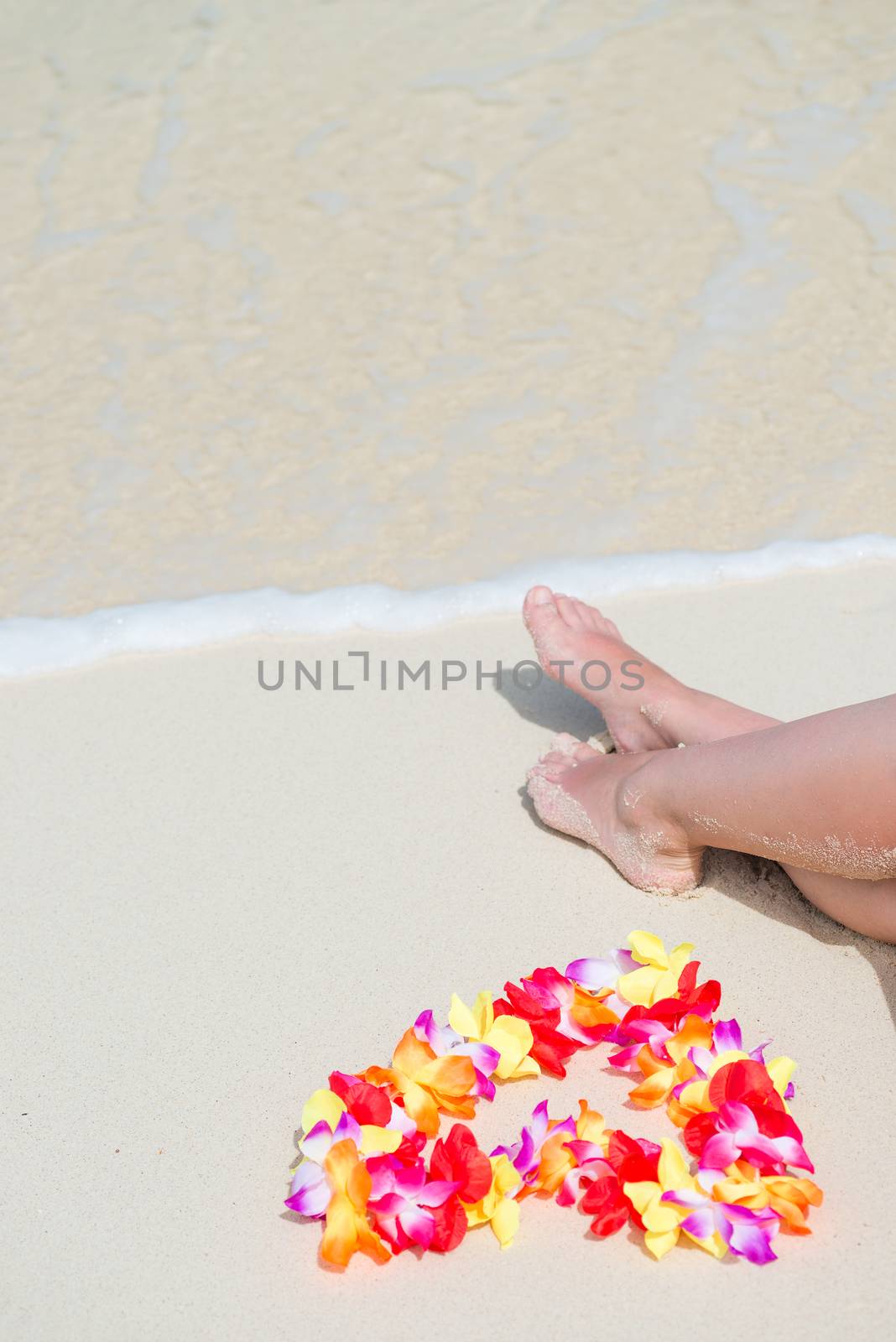 floral Hawaiian Lei in the shape of a heart near the female legs on the beach view from above