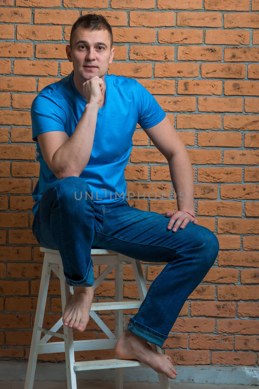 brunette in a T-shirt and jeans sits on a chair against a brick wall background