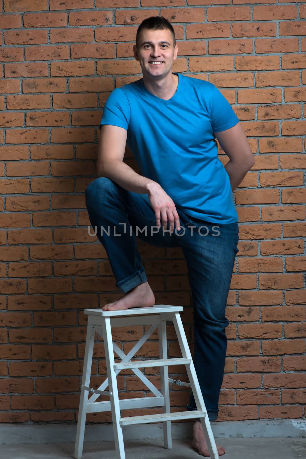 brutal barefoot man in a chair posing against a brick wall background