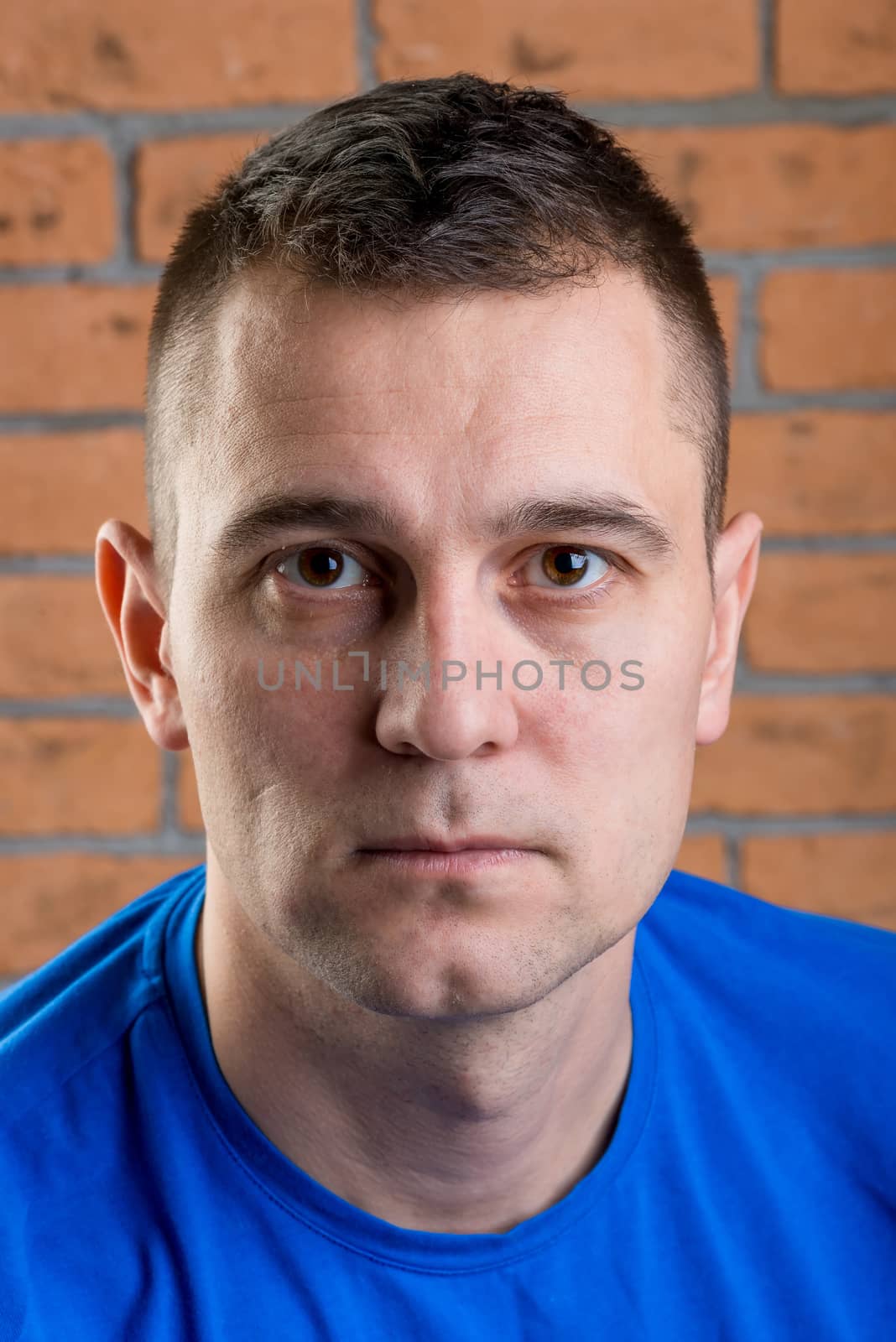 close-up portrait of a man in a blue t-shirt on a brick wall background