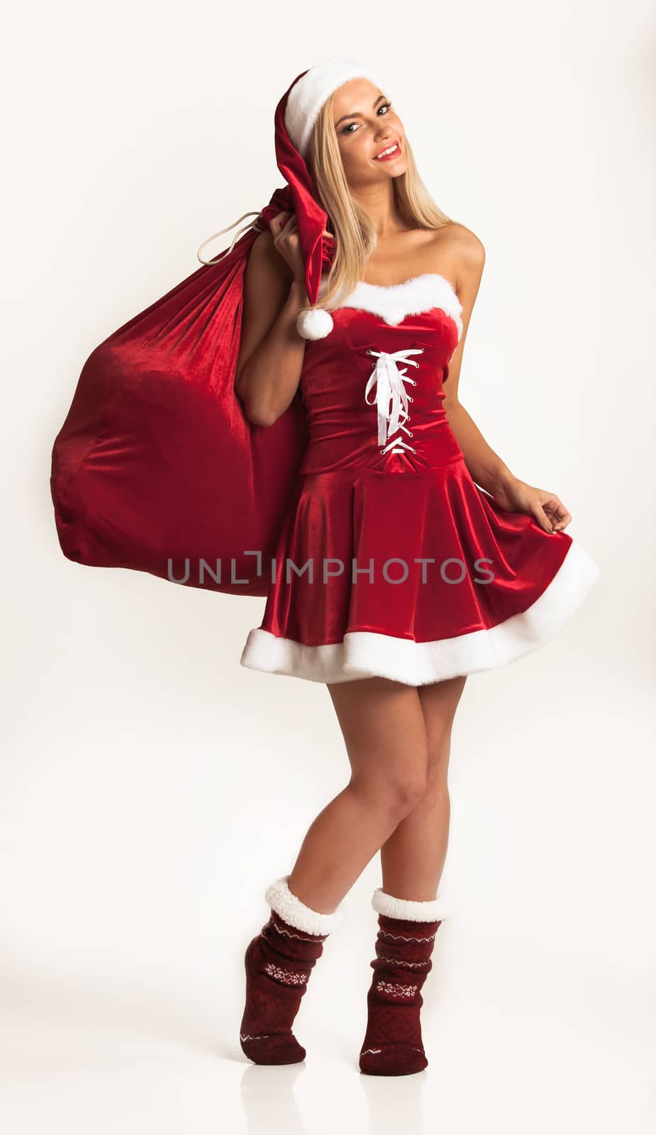 Cute young girl in santa claus costume holding large gift bag on white background