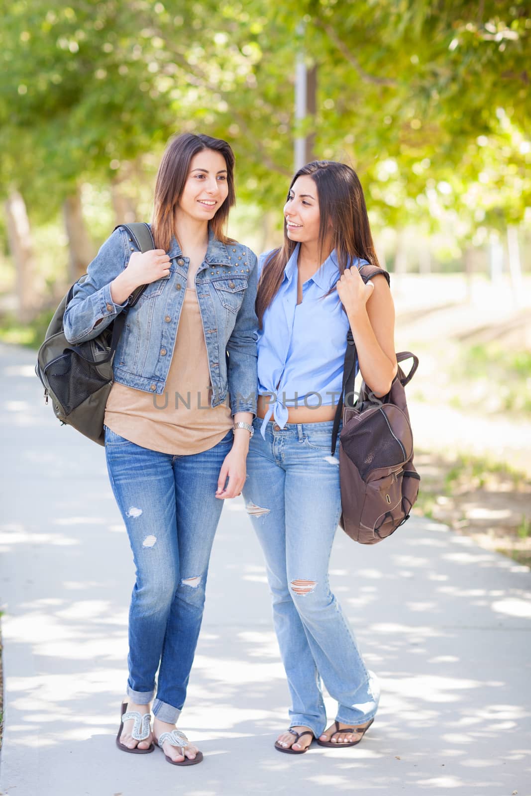 Two Beautiful Young Ethnic Twin Sisters With Backpacks Walking Outdoors.