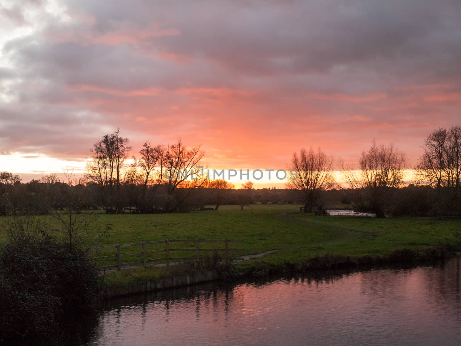 red sun setting sky dramatic autumn over empty open green countryside night dark lake; essex; england; uk