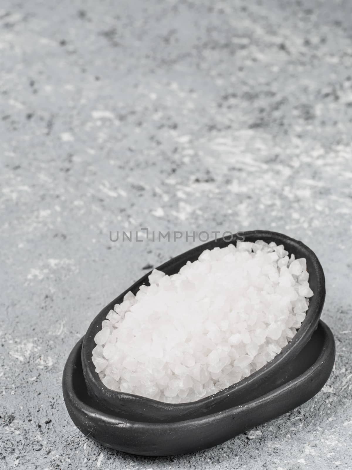 close up view of coarse sea salt ?? trendy plate on gray concrete background. Copy space.