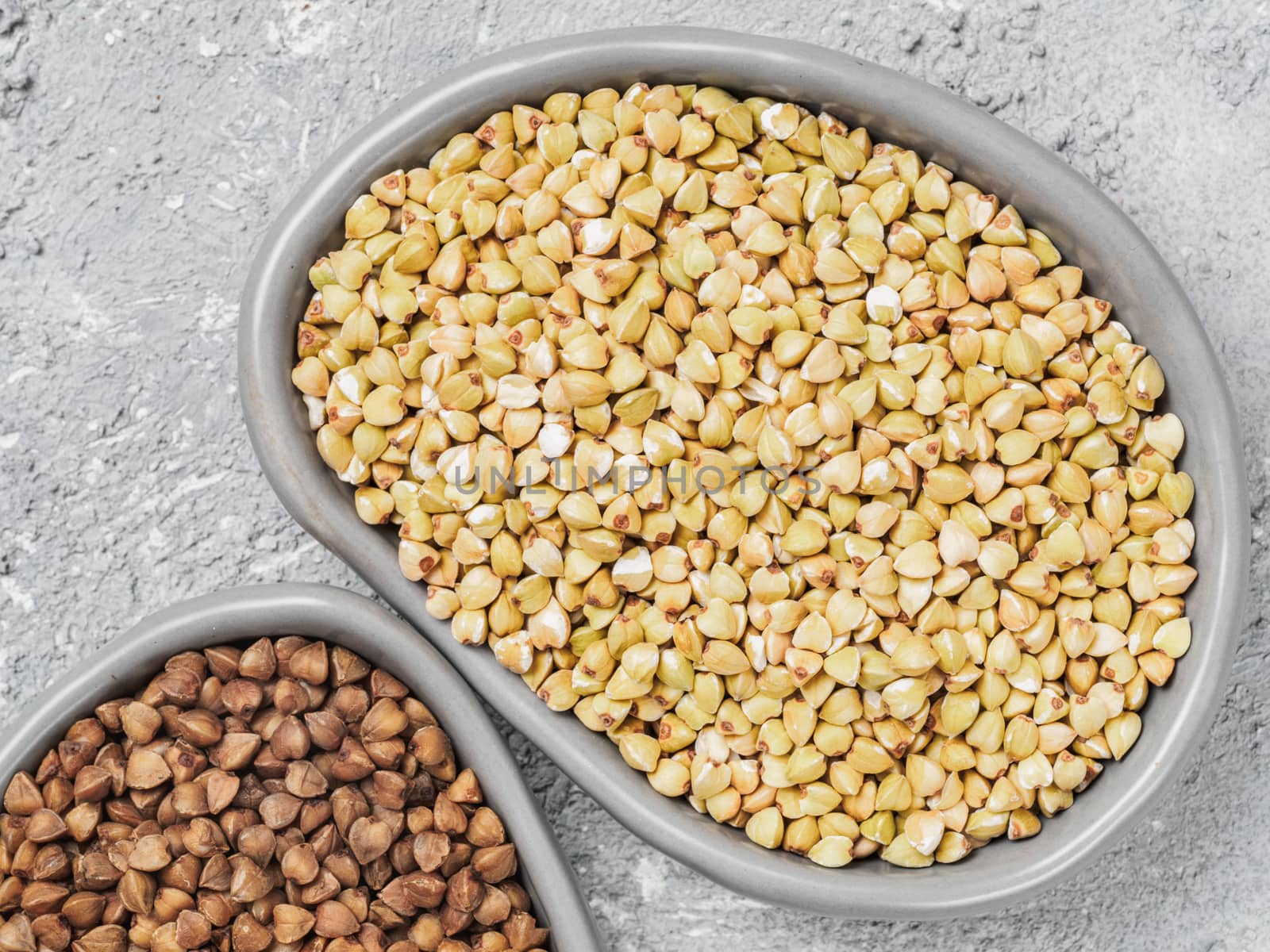 Close up view of raw green buckwheat in trandy plate and brown roasted buckwheat on background. Healthy food and diet concept. Top view or flat lay