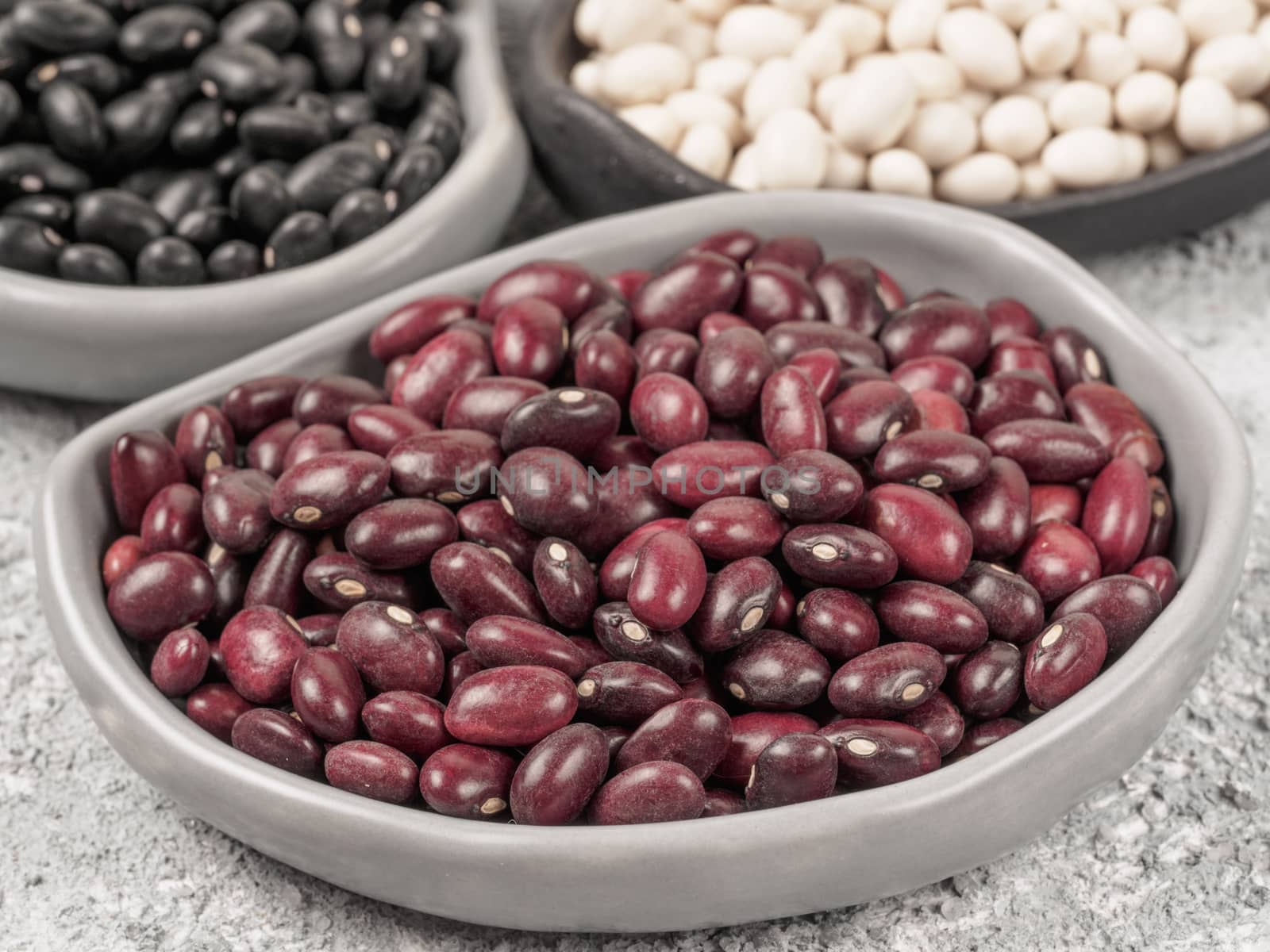 Close up view of raw red beans in trendy plate on gray concrete background. Black and white beans on background.