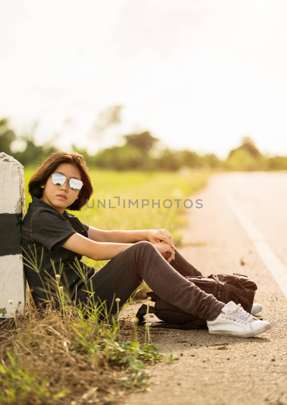 Woman sit with backpack hitchhiking along a road in countryside by stoonn