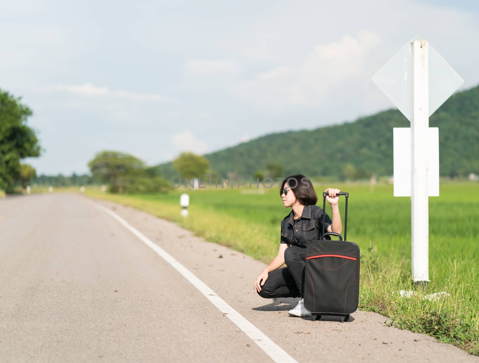 Woman with luggage hitchhiking along a road by stoonn