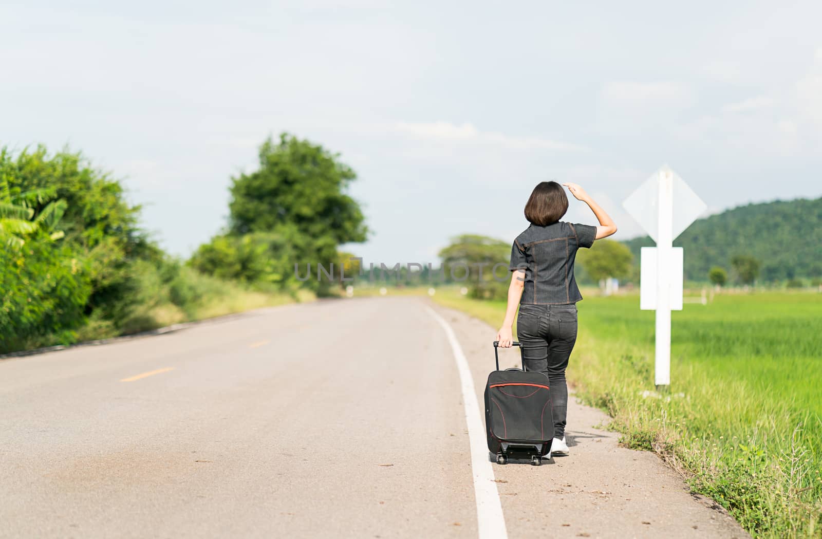 Woman with luggage hitchhiking along a road by stoonn