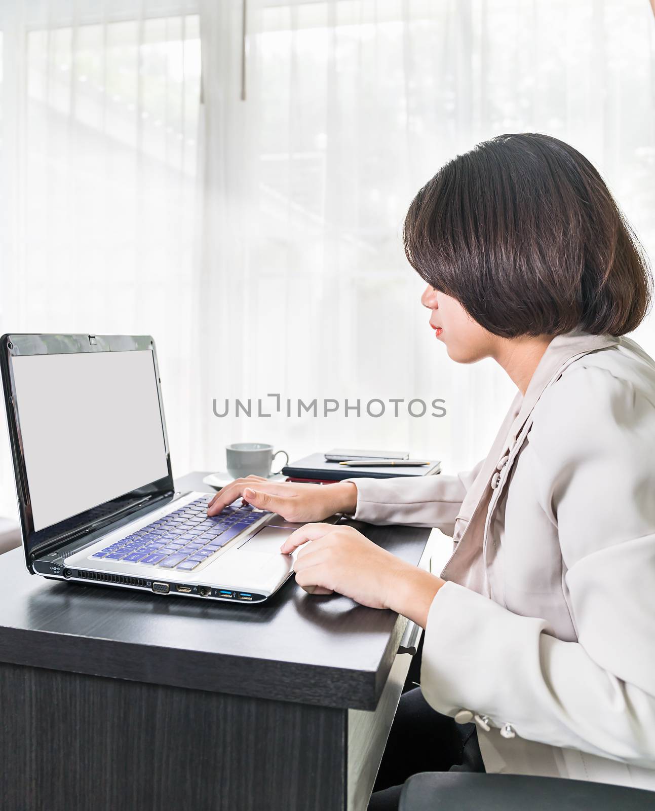 Young asian woman short hair in smart casual wear working on laptop while sitting near window in home office