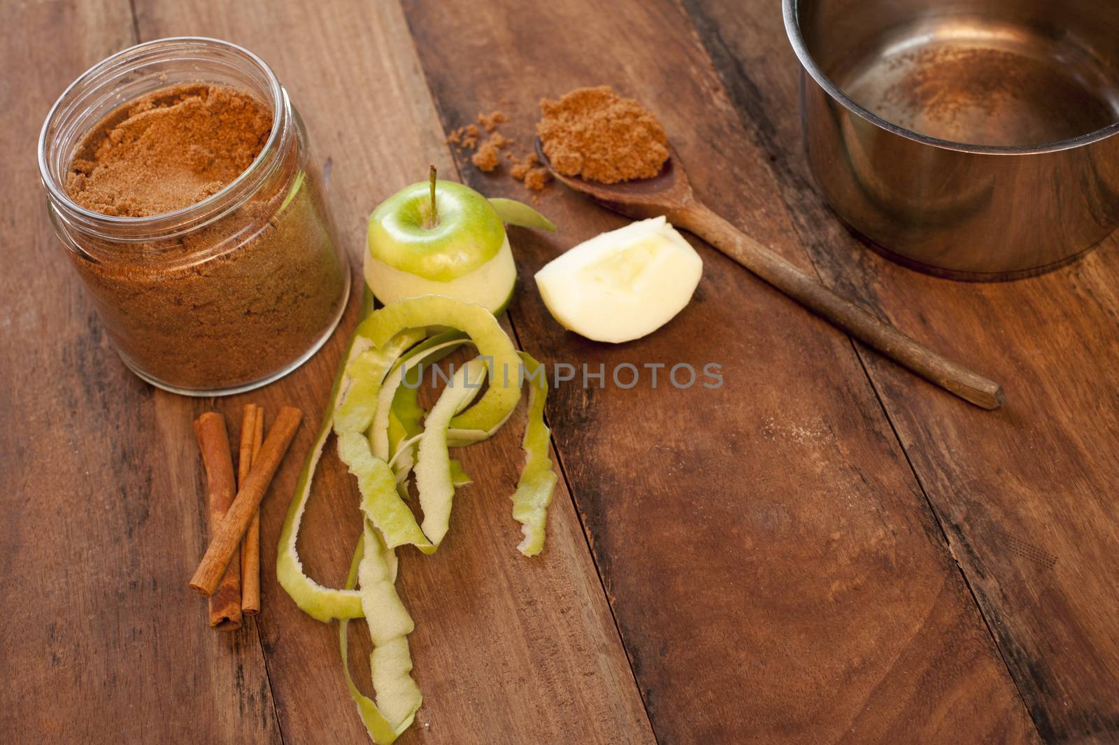 Fresh half peeled apple with aromatic cinnamon spice in the form of sticks and ground powder for use as a flavoring and seasoning in baking on a wooden kitchen table with copy space