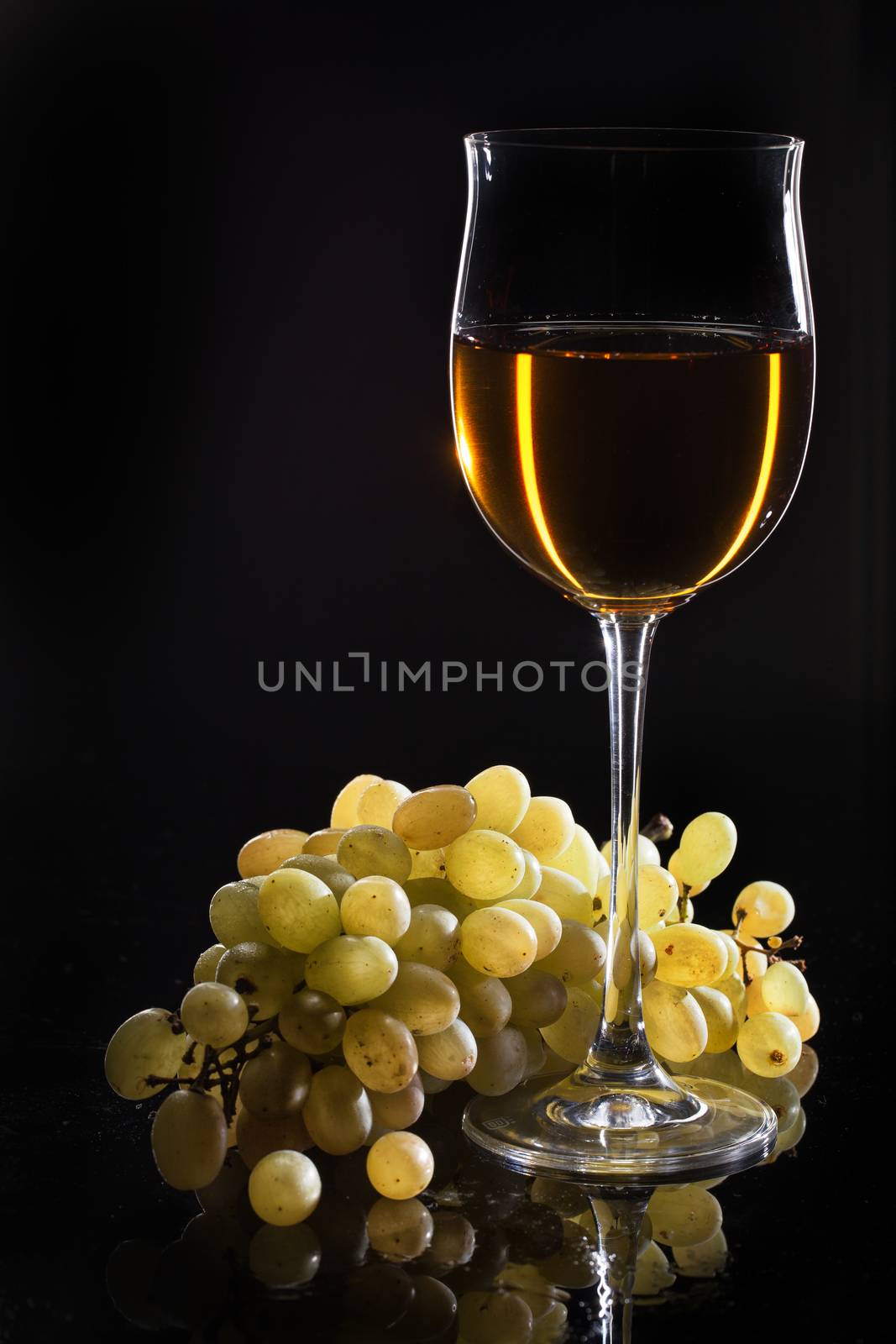 Glass of wine and a bunch of grape on a studio glass background