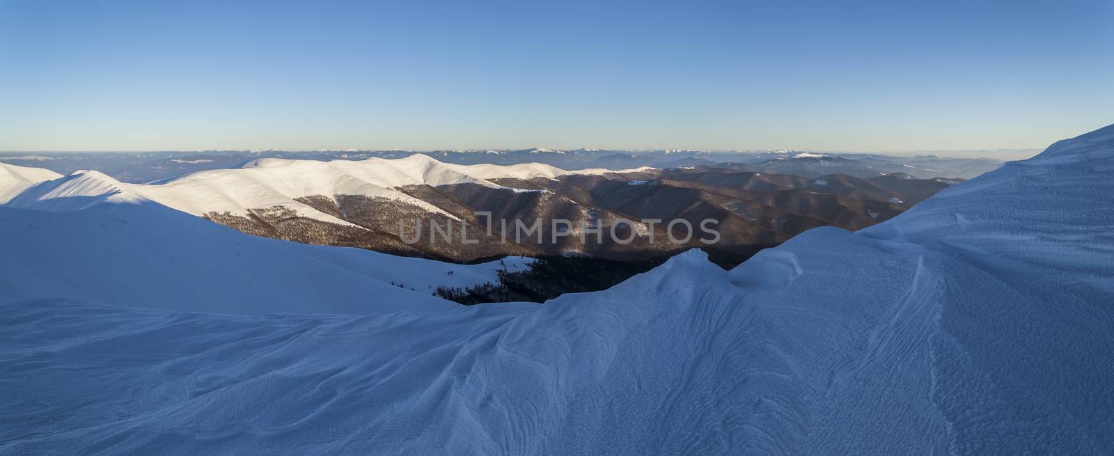 Winter in the Ukrainian Carpathians. Snowy mountain ridge. Traces of wind and frost in the snow. Wide panorama