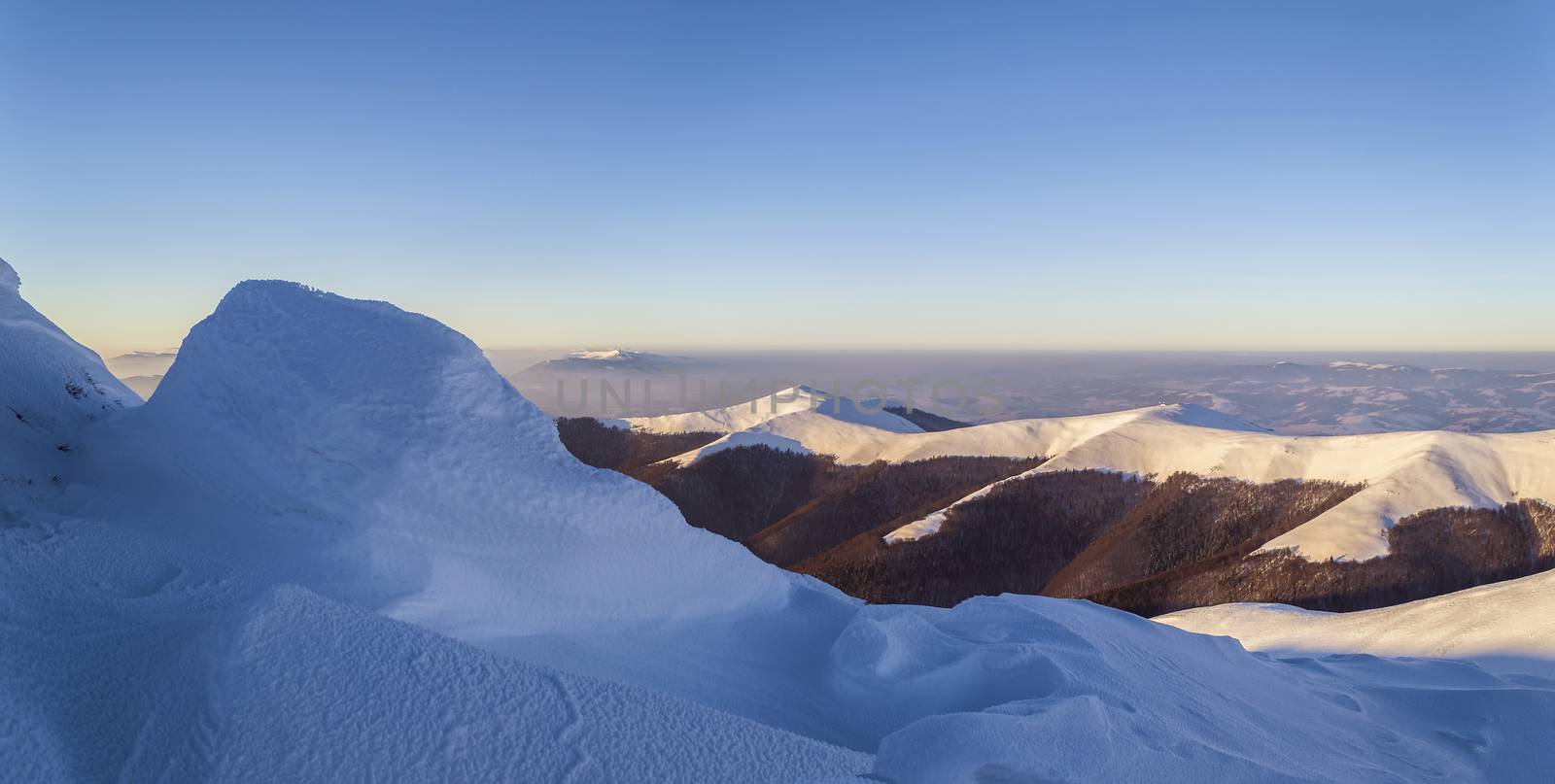 Winter evening in the Ukrainian Carpathian mountains. Gentle sunlight. Snowy mountain ridge. Snow dunes in the foreground