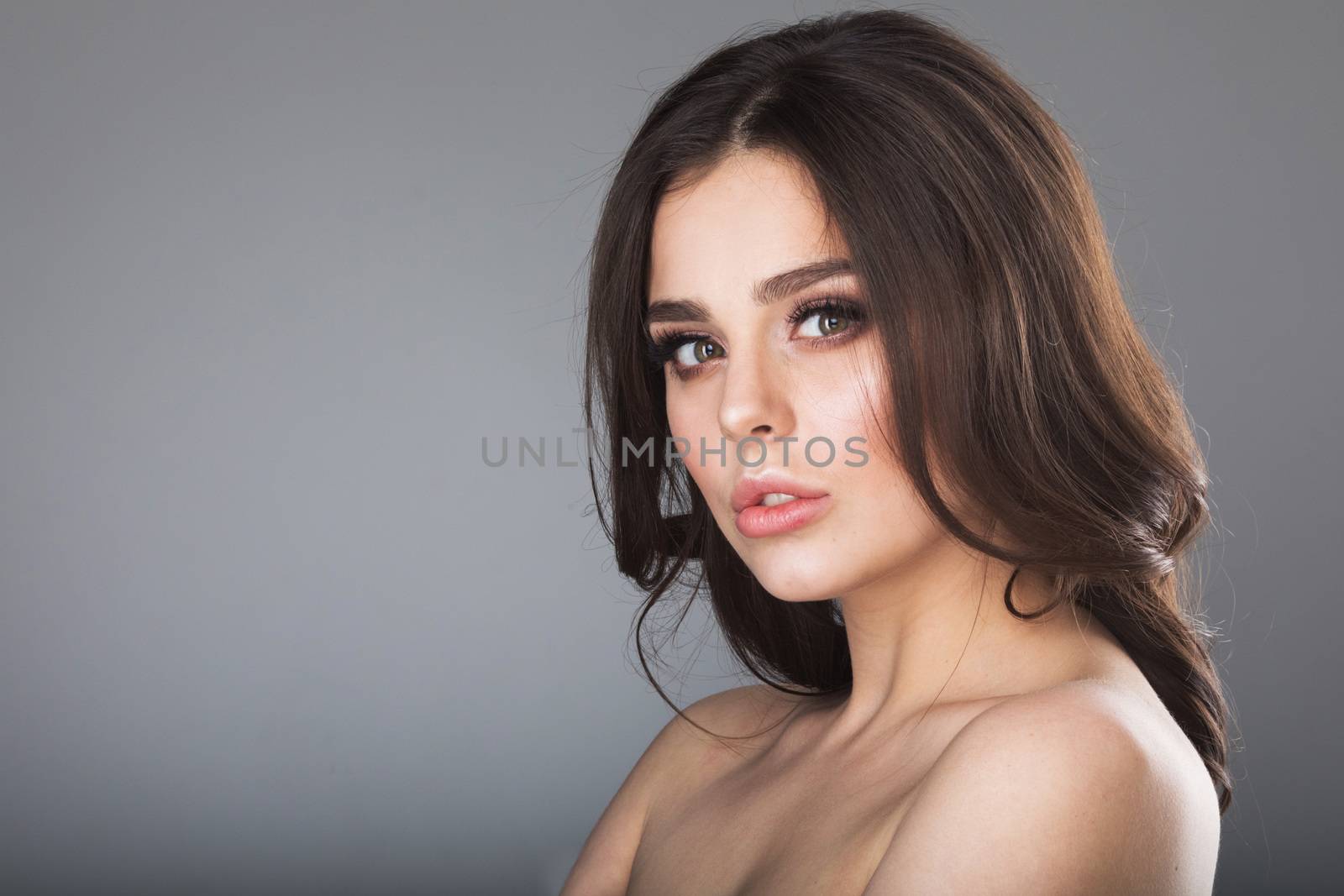 Beauty portrait of young woman with naked shoulder on gray background