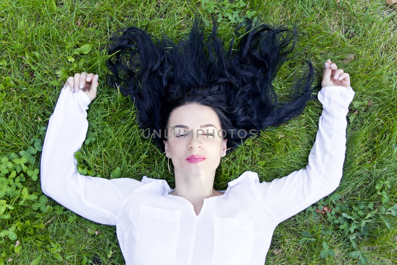 Beautiful brunette is lying on green grass in summer