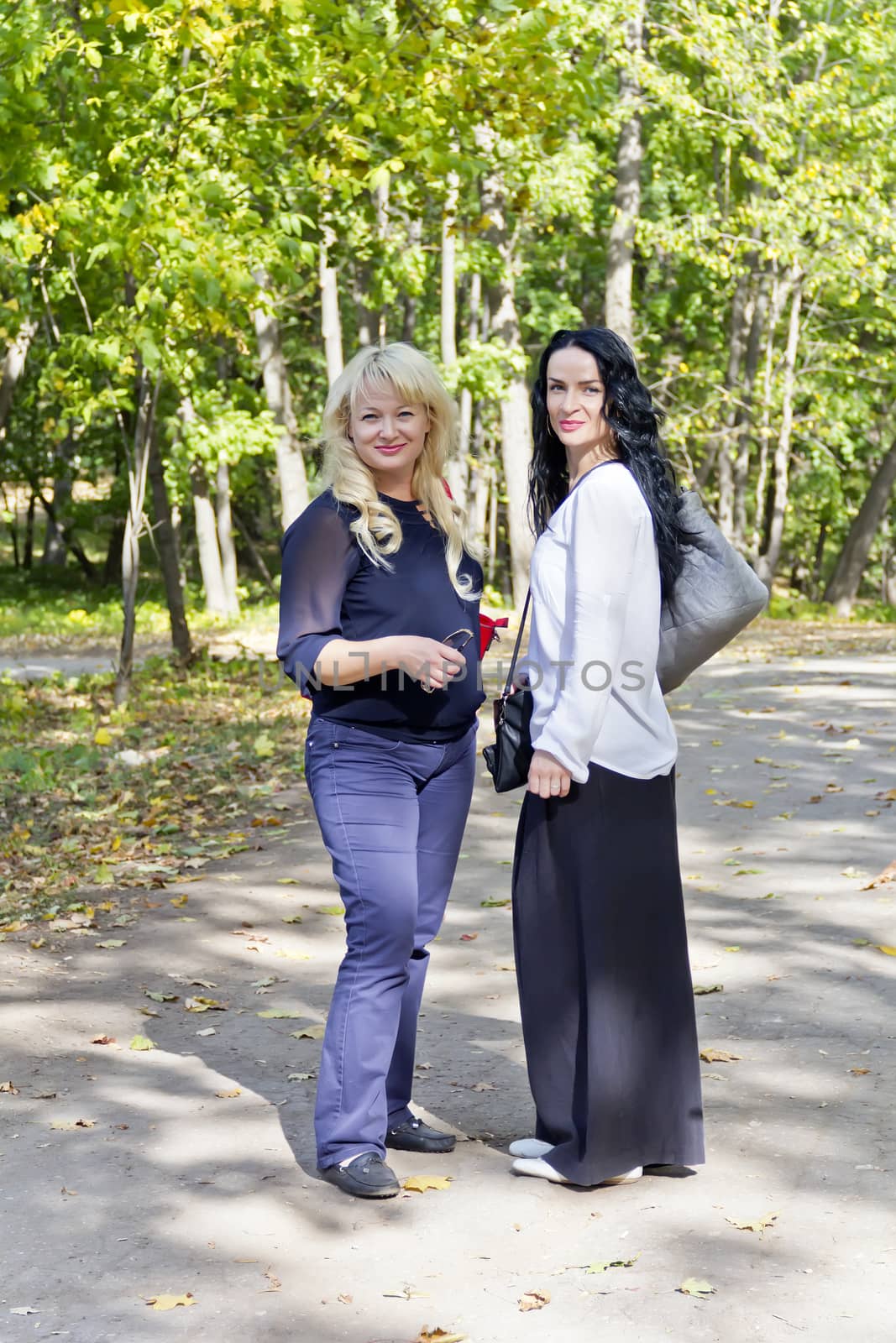 Two women blond and brunette are walking in summer day
