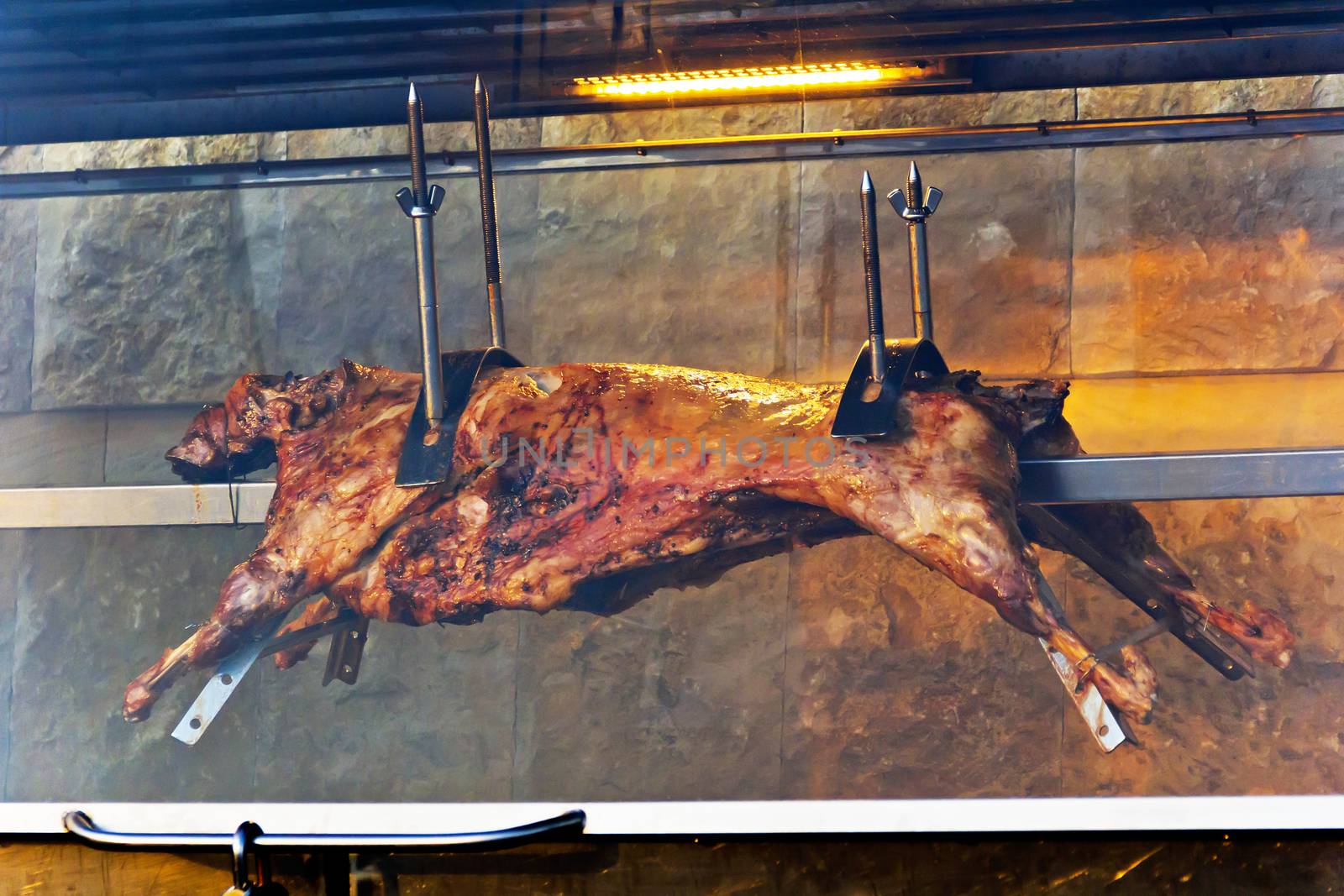 Lamb carcass on skewer behind glass in oven