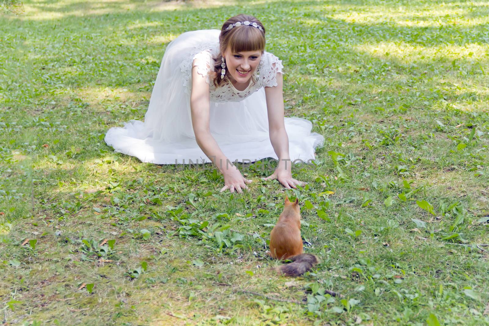 Bride in white lying on grass next to the squirrel by Julialine