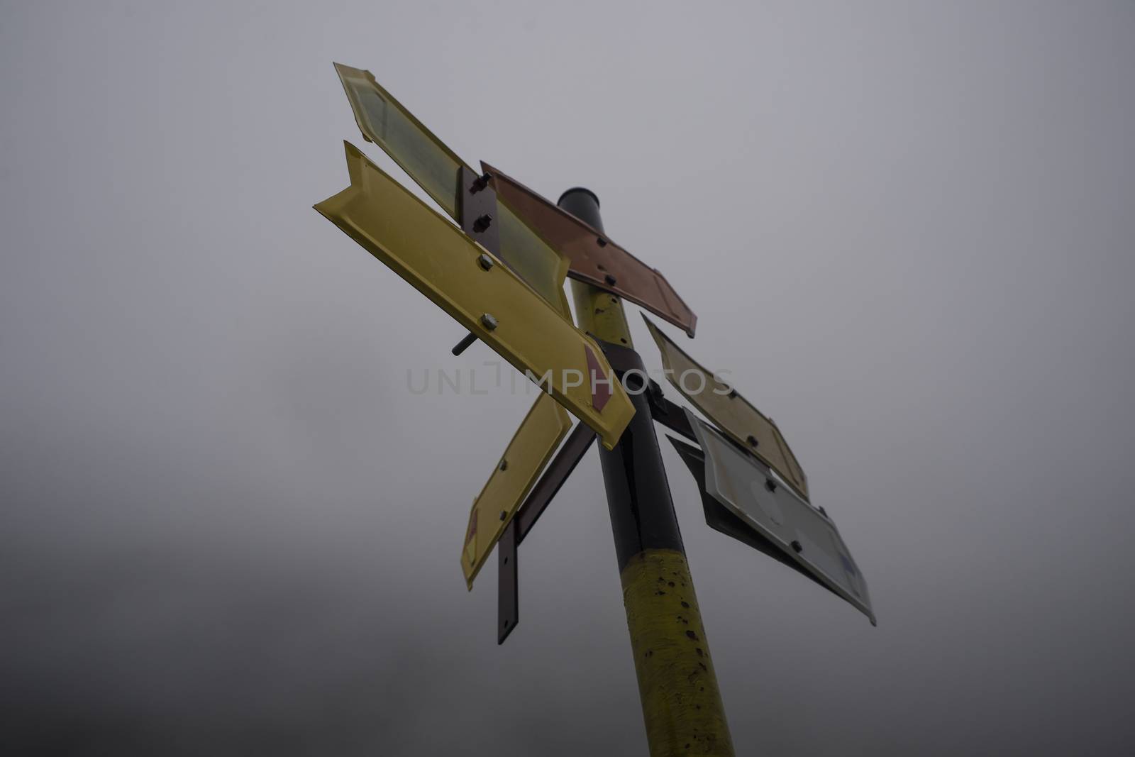 A pole with several, five usable, empty mountain road direction pointers in cold misty weather.