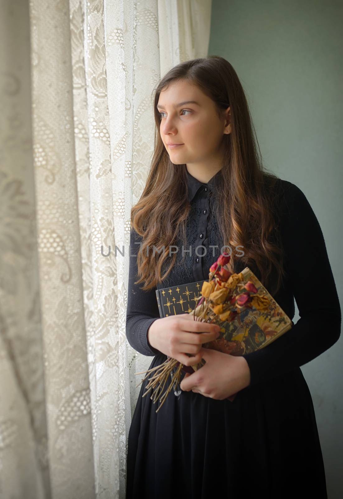 Young girl in black vintage dress standing near window 