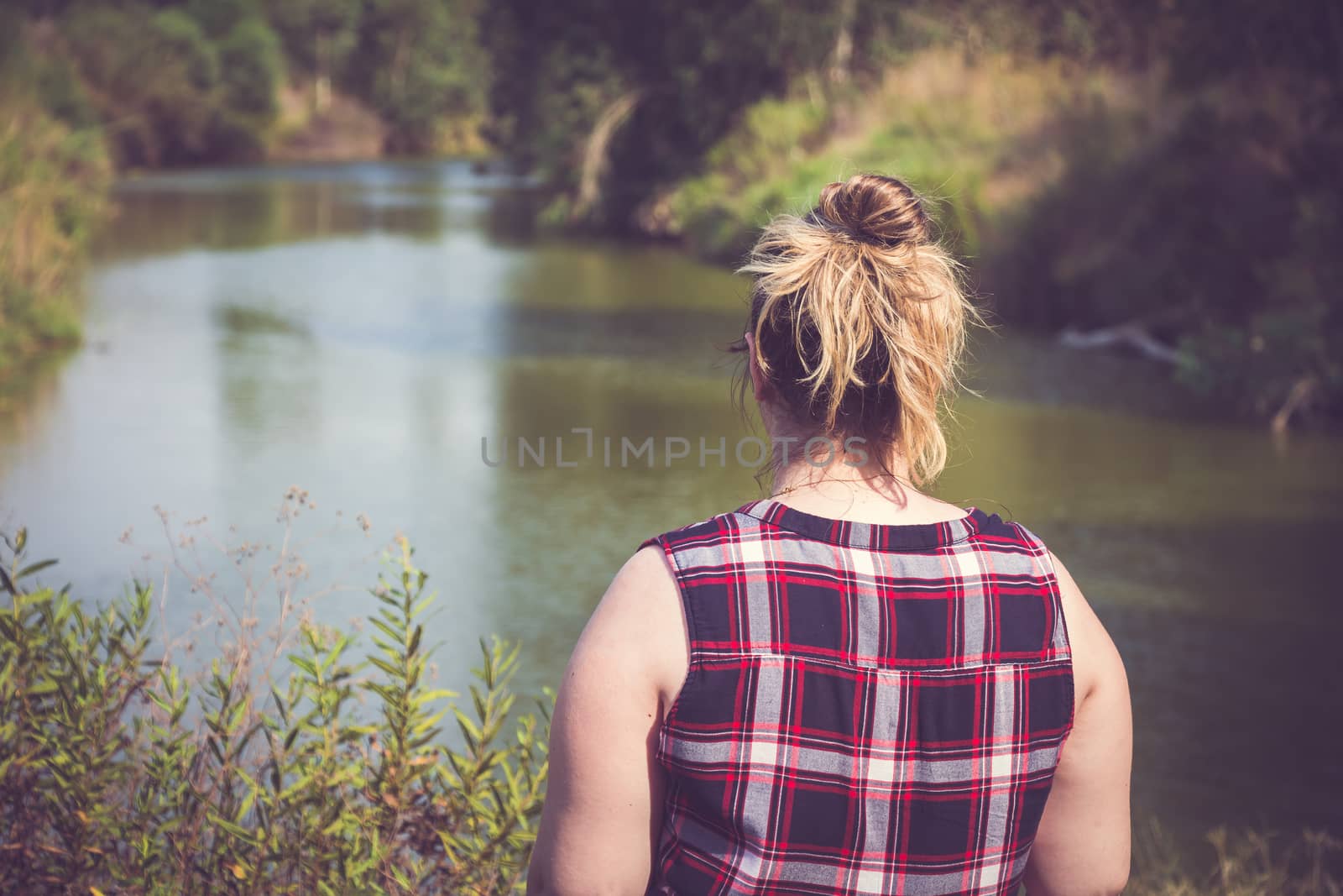 Back view of woman standing and looking away at banks of the river. Relaxation and meditation concept.