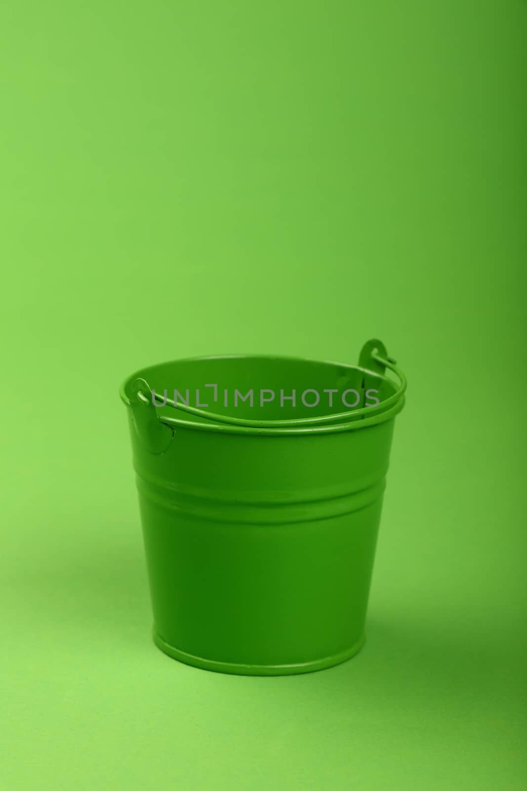 One small green painted metal empty toy bucket over green paper background, close up, high angle view