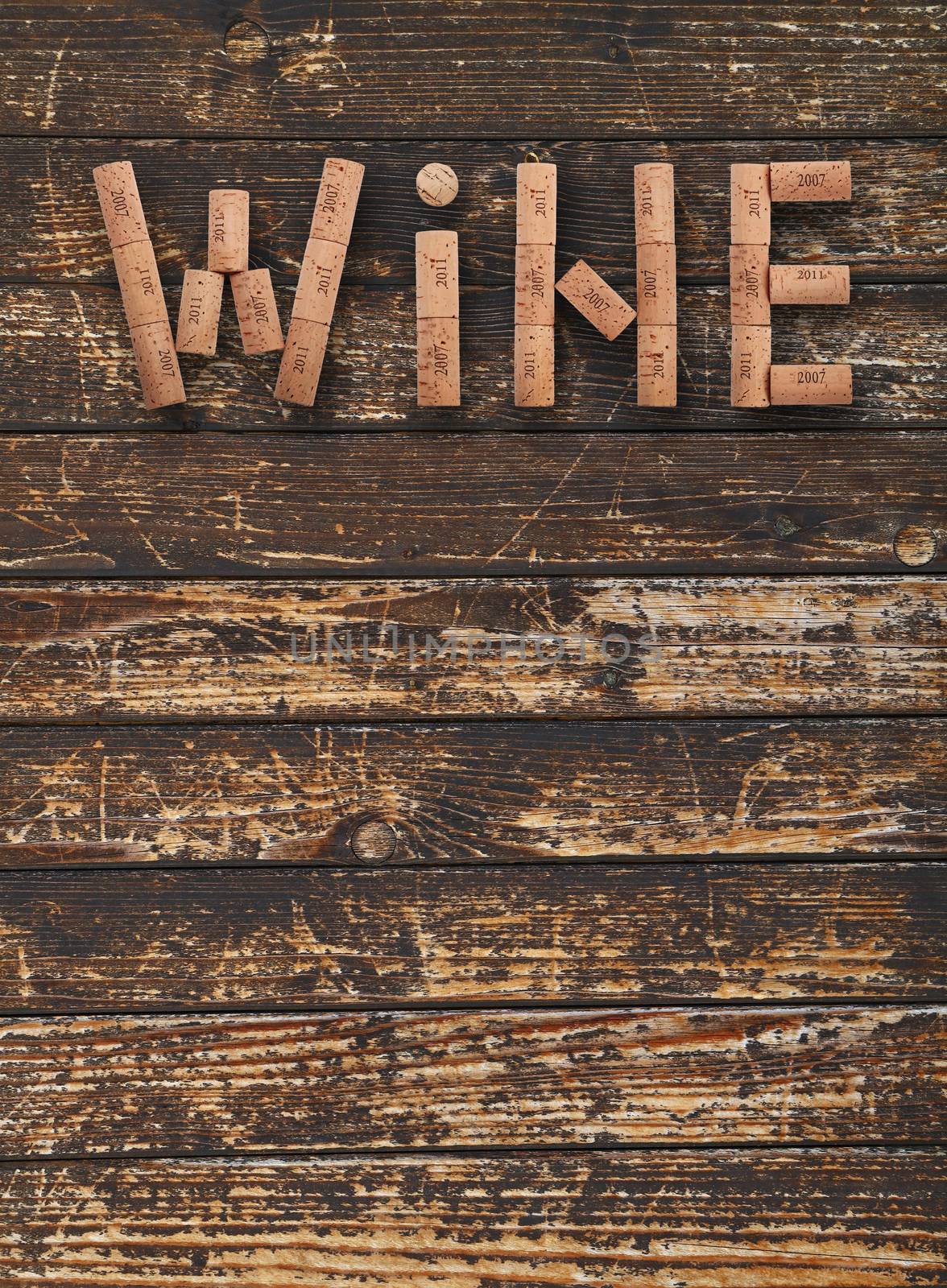Word WINE shaped by natural wooden wine bottle corks of different vintage years over background of dark old wooden planks