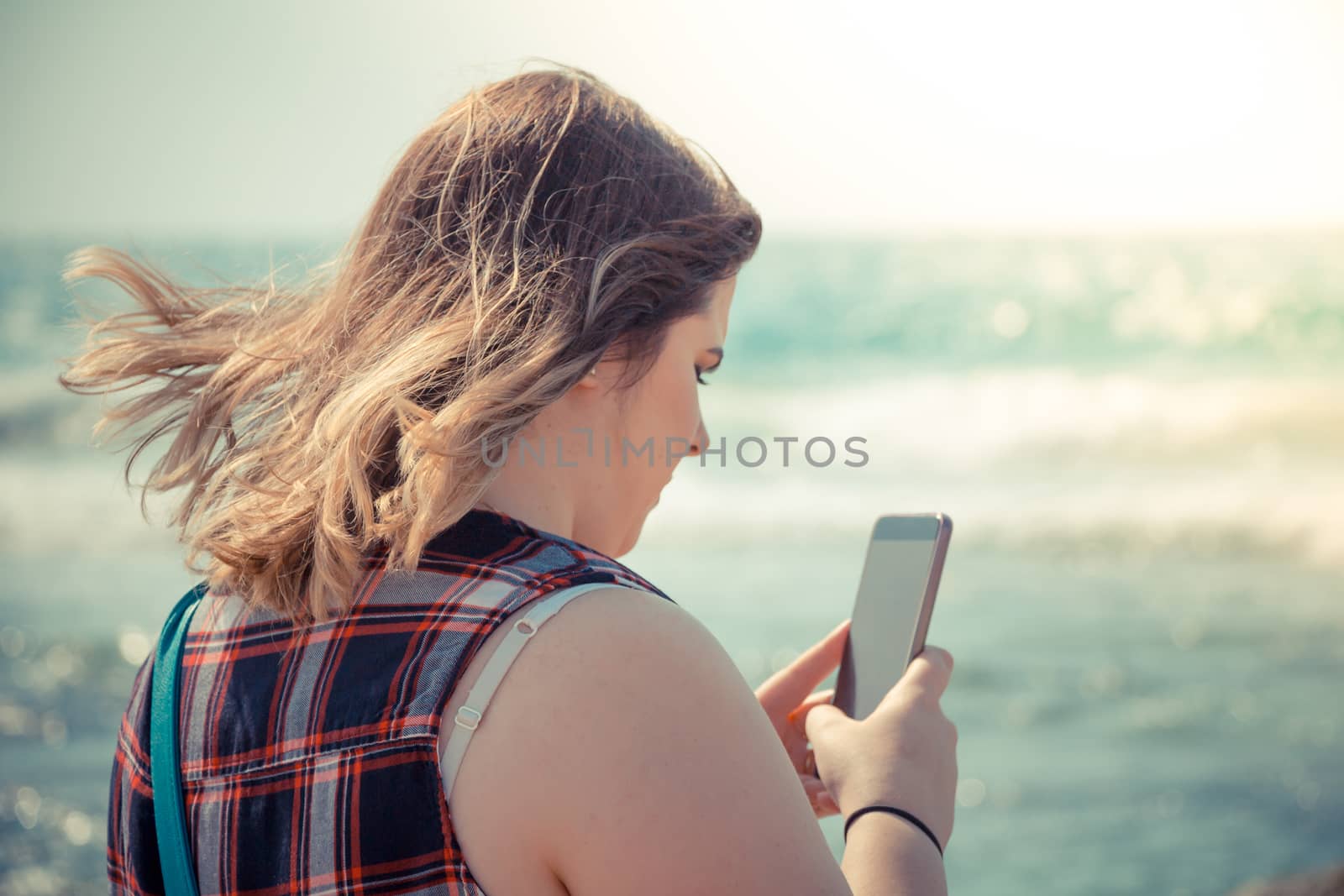 Woman using her smartphone outdoors at the beach near the sea.