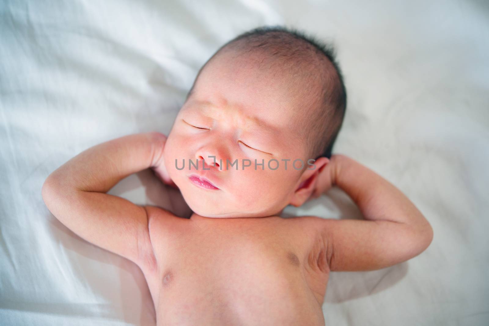 Newborn baby boy showing funny face while dreaming in bed.