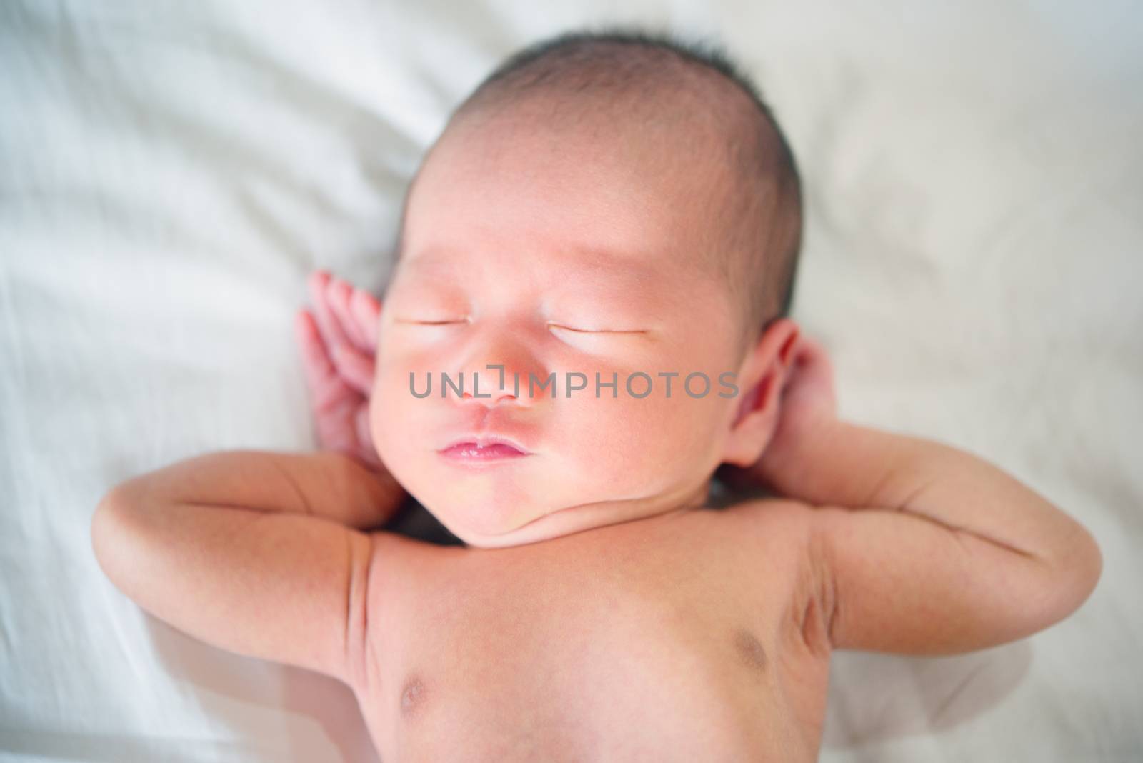 Newborn baby boy waking up and stretching in bed.