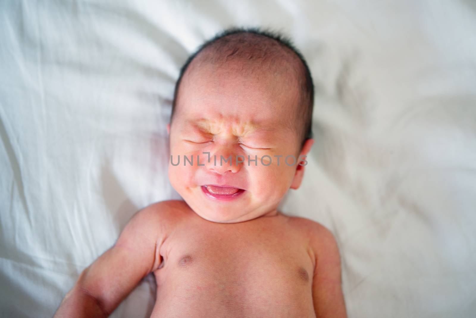 Asian newborn crying baby boy. 7 days old new born child tired and hungry in bed. 