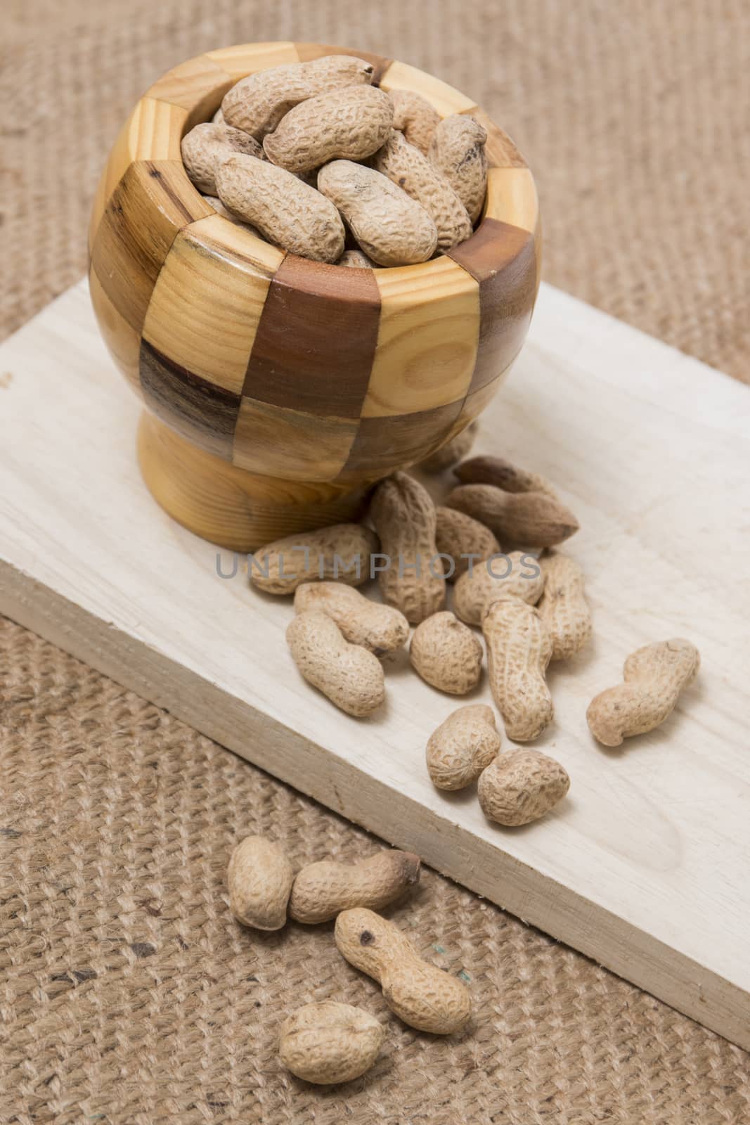Bowl of peanuts over a wooden board and hessian fabric.