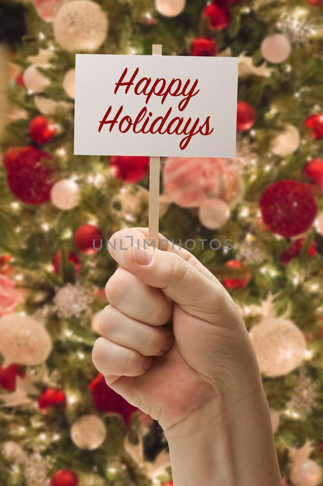 Hand Holding Happy Holidays Card In Front of Decorated Christmas Tree.