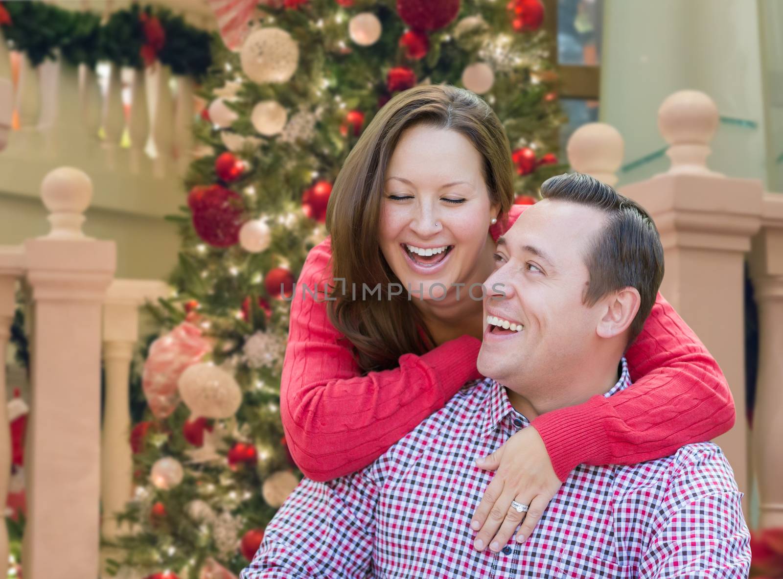 Caucasian Couple Laughing In Front of Decorated Christmas Tree.